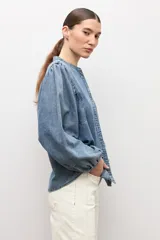 Camisa de jean de corte clásico con cuello mao, cierre frontal con botones y mangas largas abullonadas con puños elásticos.