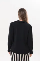 Camisa de manga larga color negro, con cuello camisero, cierre frontal con botones y detalle de volados en la cartera y los puños.