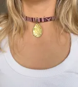 Gargantilla con cinta de tela estampada en tonos marrón y blanco, con dije dorado en forma de gota.