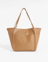 Bolso tipo shopper color marrón claro, de cuero sintético, con doble asa larga para llevar al hombro y bolsillo externo. Incluye estuche interno extraíble.