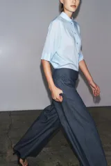 Camisa de color mostaza, con cuello solapa, manga corta y bajo recto. Cierre frontal con botones.