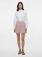 Pollera corta de tiro alto confeccionada en tejido tweed con estampado a cuadros en tonos rosados y negros. Presenta un ruedo con volado.