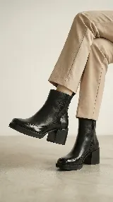 Bota corta de cuero negro con acabado brillante, diseño minimalista, taco cuadrado medio y plataforma delantera. Cuenta con cierre lateral interno para facilitar el calce.