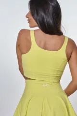 Conjunto deportivo compuesto por un top de escote redondo con logo estampado y una pollera short con diseño plisado, ambos en color amarillo.