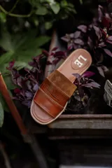 Sandalias planas de cuero marrón con tira ancha sobre el empeine. La plantilla es de cuero con la inscripción "LE".