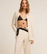 Pantalón recto de cintura alta, color beige, confeccionado en viscolino con detalle de textura perforada con diseño de palmeras en el bajo. Cuenta con elástico en la parte posterior de la cintura y cierre frontal tradicional.