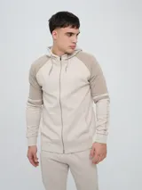 Campera deportiva con capucha de color beige y marrón claro, con cierre frontal completo, bolsillos tipo canguro y bandas laterales decorativas en las mangas.