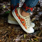 Sneakers de cuero color natural con diseño artístico pintado a mano en tonos rojos y naranjas en los laterales, pas cordones al tono y suela blanca.