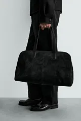 Bolso de viaje de diseño minimalista confeccionado en piel con acabado serraje. Cuenta con compartimento principal con cierre de cremallera e imanes, interior con bolsillos organizadores y doble asa de mano en piel.