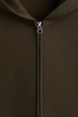 Campera con capucha y cierre frontal, color verde oscuro, de corte holgado y hombros caídos. Posee bolsillos delanteros abiertos.