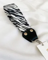 Llavero de tela con estampado de cebra, con detalles en cuero sintético negro y gancho metálico plateado.