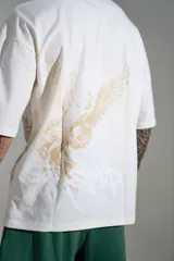 Remera oversize de algodón color off-white, con mangas cortas amplias y cuello redondo. Presenta un pequeño estampado en el centro del pecho y un diseño gráfico más grande en el lateral inferior.