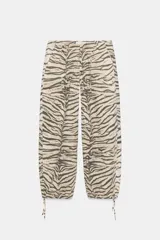 Pantalón de tiro medio con estampado animal print tipo tigre en tonos beige y negro. Presenta trabillas, cintura ajustable con cordones, bolsillos laterales y traseros, y bajo ajustable con cordón. Cierre frontal con cremallera y botón a presión.