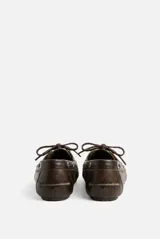 Mocasin acordonado de color chocolate con costuras visibles y detalles de ojales metálicos.