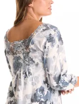 Blusa de tejido estampado con diseño floral en tonos grises y blancos, con escote redondo decorado con aplique de encaje y mangas tres cuartos tipo raglán.