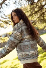 Campera de jean con cierre frontal y cuello tipo bomber, presenta un estampado horizontal con motivos paisajísticos y geométricos en tonos azules, marrones y beige. Posee puños de tela elástica en color blanco.