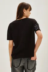 Remera negra de manga corta con cuello redondo, decorada con apliques de lentejuelas azules y doradas dispuestas en forma de explosión o rayos.
