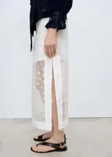Falda midi de tiro medio con diseño recto y semitransparente. Presenta un delicado bordado de flores con detalles en amarillo y una abertura lateral en el bajo. Incluye forro interior y cierre de cremallera lateral.