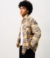 Camisa masculina de algodón con diseño a cuadros, corte oversized, cuello camisero, bolsillos frontales con solapa, cierre de botones y estampa en las mangas.