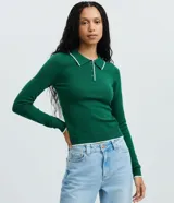Blusa de punto manga larga de color verde con cuello polo y cierre frontal de botones. Presenta detalles de ribetes blancos en el cuello, puños y dobladillo.