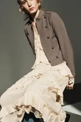 Vestido midi de escote en pico con lazada frontal y diseño sin mangas. Presenta múltiples niveles de volantes a lo largo de la falda y cierre lateral con cremallera oculta.