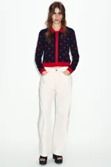 Chaqueta de punto jacquard en color azul marino con estampado de corazones rojos. Presenta cuello de solapa, manga larga y cierre frontal con botones rojos en forma de corazón. Los puños, el cuello y el bajo son de color rojo liso.