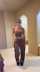 Pantalón marrón de gamuza con flecos laterales y ajuste con cordones en la cintura.