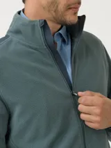 Campera polar de poliéster reciclado color verde, con cierre frontal completo, cuello alto y detalles de tela en los hombros y bolsillos.