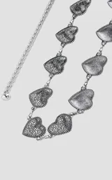 Cinto de cadena metálica plateada compuesto por eslabones en forma de corazón con detalles grabados en relieve.