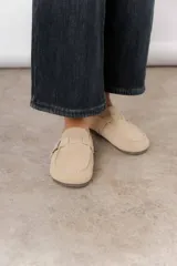 Zueco de cuero gamuzado color marrón, con diseño minimalista y elegante. Cuenta con una tira lateral con hebilla metálica regulable y plantilla acolchada. Su base es liviana y flexible.