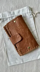 Set de accesorios compuesto por un brazalete rígido abierto, un collar con dije de sol radiante, un par de caravanas onduladas y un par de caravanas tipo fleco, presentados en un sobre de cuero con costuras artesanales.