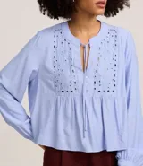 Blusa tipo bata de color celeste con mangas largas y cuello mao con lazo. Presenta detalles de bordado floral calado tipo laise en el frente y cierre parcial con botones.