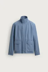 Cazadora de algodón lavado en color azul, corte regular fit, con cuello subido, bolsillos frontales de plastrón con solapa y cierre frontal de cremallera oculta con solapa de botones a presión.