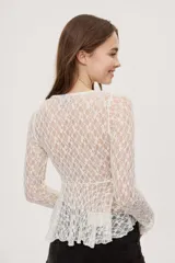 Top de encaje negro semitransparente con escote en V profundo, volados en los bordes y mangas largas. Cuenta con cierre frontal con lazos para anudar y diseño irregular.