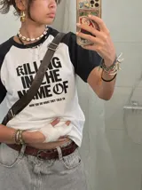 Remera oversize de corte raglan, color blanco con mangas y cuello en contraste negro. Presenta estampado frontal con la inscripción "KILLING IN THE NAME OF" y el texto secundario "NOW YOU DO WHAT THEY TOLD YA".
