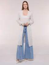 Cardigan largo de punto liviano y suave, de color blanco, con diseño abierto al frente, mangas largas con puños acanalados y bolsillos frontales aplicados.