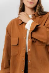 Sobrecamisa de gabardina liviana color crema, con corte oversize, cuello clásico, cierre frontal con botones a presión y dos bolsillos delanteros con solapa.