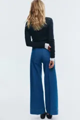 Pantalón de jean de tiro alto, color azul medio, con pierna ancha y corte ajustado en la cadera. Presenta bolsillos de parche tanto en la parte delantera como en la trasera.