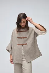 Capa de lana fina sin teñir, con diseño de corte amplio y mangas tipo kimono. Presenta cierre frontal mediante tres alamares de cuero en tono marrón.