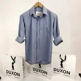 Camisa de manga larga a rayas verticales celestes y blancas, con cuello italiano y logo bordado en el pecho.