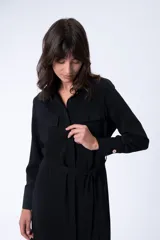 Vestido camisero midi negro con cuello camisero, mangas largas, dos bolsillos en el pecho, cinturón de lazo y abertura lateral.