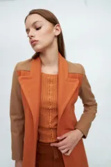 Tapado largo de paño con diseño combinado, presentando cuerpo en color naranja y mangas en tono marrón. Posee solapas clásicas, cierre frontal y un corte recto y estructurado.