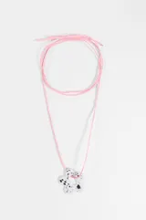 Collar largo con cordón de gamuza sintética color rosado y dije colgante en forma de flor blanca con estampado efecto salpicado en negro.
