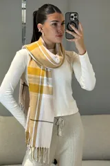 Bufanda rectangular de tejido suave con diseño de cuadros escoceses en tonos mostaza, blanco y gris, terminada con flecos en los extremos.