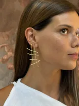 Caravanas largas de bronce con diseño geométrico de líneas cruzadas.