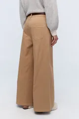 Pantalón de vestir color crema, de corte ancho y tiro alto. Se ajusta a la cintura con cinturón de cuero marrón.