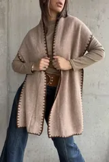 Ruana abierta de tejido de punto en color beige, con bordes terminados en punto festón de color marrón oscuro.