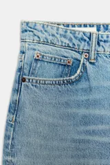 Jeans de tiro alto con corte mom fit, confeccionados en denim de lavado claro. Presentan diseño clásico de cinco bolsillos, trabillas para cinturón y cierre frontal con cremallera y botón metálico.