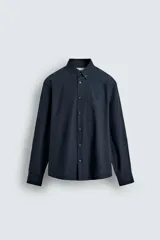 Camisa de corte regular fit confeccionada en tejido de algodón. Presenta cuello con solapa abotonada, cierre frontal con botones, manga larga con puños abotonados y un bolsillo plastrón en el pecho.