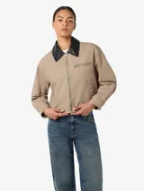 Chaqueta estilo worker de gabardina en color beige, con cuello camisero de cuerina negra, cierre frontal de cremallera y bolsillos frontales con cierre y ribete.